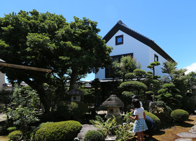 改修された蔵を母屋から日本庭園越しに見る
